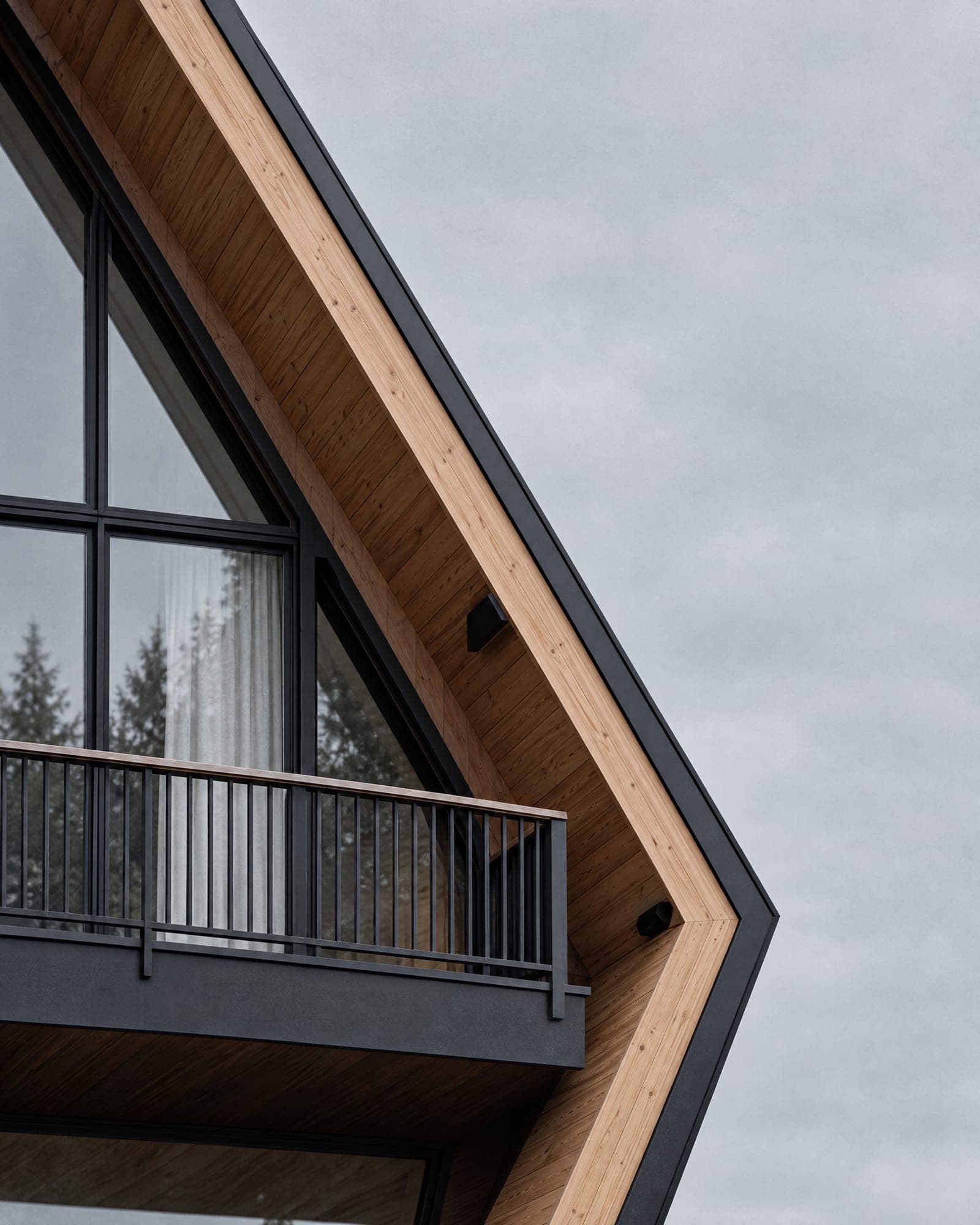 Close view of the knee of an AFRME roof where the black standing-seam metal folds inward against the pale larch reveal