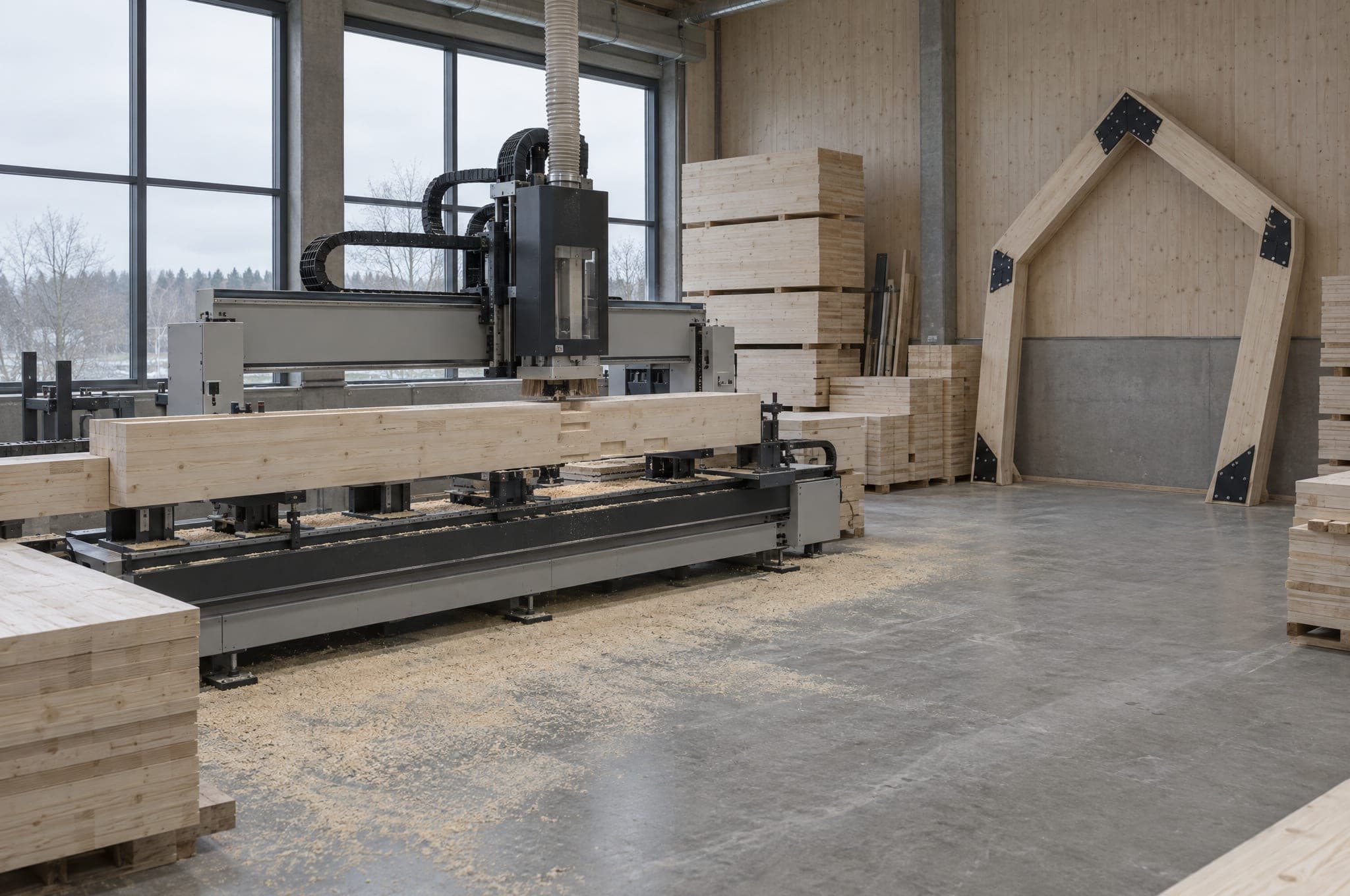 A CNC joinery machine cutting a laminated timber beam in the AFRME workshop, a finished frame leaning against the wall