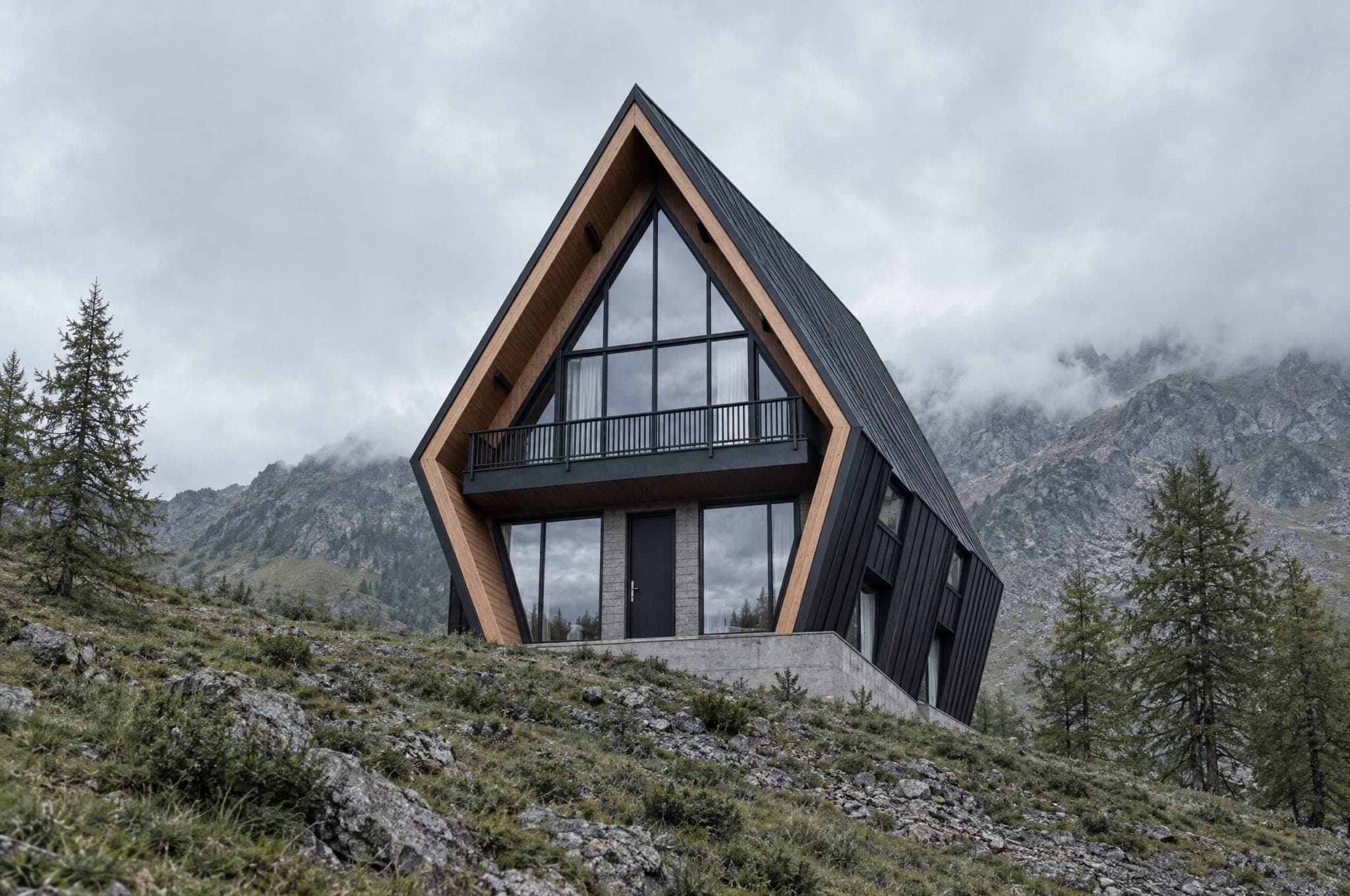 The Three, a tall three-story A-frame with a gable balcony, on a steep alpine meadow with cloud on the ridge